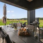 Moderne schwarze Holzhütte mit großem Glasbereich und Terrasse im Gras.