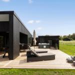 Moderne schwarze Villa mit Spielplatz und grünem Rasen unter blauem Himmel.