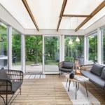 Interior with glass walls, wooden floor, and seating. View of green garden.