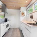 Modern kitchen with white cabinets, stainless steel sink, and wooden ceiling.
