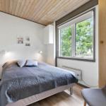 Bedroom with bed, window, and chair. Wooden ceiling and white walls.