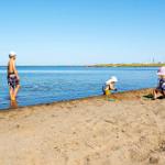 Two people wade in shallow water, a boat sails through a canal.