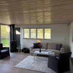 Wohnzimmer mit Sofa, zwei Sesseln, Kamin und Blick auf Garten.
