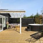 Deck with hot tub, seating area, and lawn. Black wood walls and wooden planks.