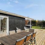 Deck with wooden table and chairs, adjacent garden and holiday home with glass doors.
