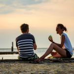 A couple sits by the waters edge enjoying ice cream in the evening.
