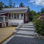 House with terrace, bench, and steps to entrance. Surrounded by greenery and flowers.
