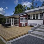 Deck with table, chairs, and sofa in front of a house with red wood siding and white windows.