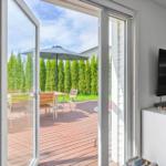 Durch Glastüren ist eine Terrasse mit Tisch, Stühlen und Sonnenschirm zu sehen.