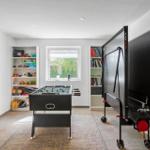 Raum mit Tischfußball und aufstellbarem Tischtennis-Tisch. Bücherregale und Fenster mit Blick auf Garten.