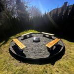 Runder Feuerplatz mit vier Holzbänken und Zentralfeuer im Garten.