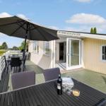 Terrasse mit Tisch, Stühlen und Sonnenschirm. Weißes Geländer und grüne Bäume im Hintergrund.