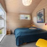 Schlafzimmer mit Holzwand, großem Fenster und blauer Bettdecke.