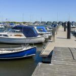 Terrasse mit Tischen und roten Sonnenschirmen am Wasser. Boot liegt an Pier.
