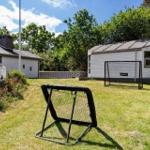Backyard with soccer goal and small house. Grass area and trees in the background.