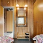 Zimmer mit Holzwand, Spiegel, Schuhschrank und zwei Betten mit Blumenbezügen.