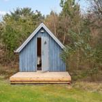Ein kleines blaues Holzhaus mit offener Tür auf einer Holzterrasse im Wald.