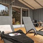 Terrasse mit zwei Liegestühlen, Holzdielen und Glasfront zur Unterkunft.