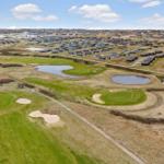 Golfplatz mit Bächen und Sandbunkern. Hintergrund: Ferienhäuser und Landschaft.