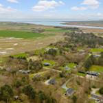 Aerial view of rural area with houses, green fields, and coastal waters.