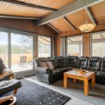 Wohnzimmer mit Leder-Sofa, Sessel und Holztisch. Große Fenster und Terrasse.