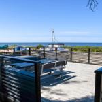 Deck with tables and benches offers view of sea and boats.