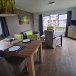 Wohn- und Essbereich mit Tisch, Stühlen, Sofa und TV. Holzdielen und große Fenster.