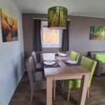 Essbereich mit Tisch, Stühlen und Sofa. Wandbilder und Hängelampe sind sichtbar.