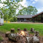 Haus mit Grillplatz und Feuerstelle im Garten. Holzstapel um Feuer. Terrasse mit Sitzgelegenheit.