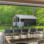 Terrasse mit Tisch und Stühlen, Blick auf Holzschuppen und grünen Garten.