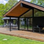 Moderne Villa mit Holzterrasse, Sitzgelegenheiten und Grillbereich im Grünen.