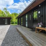 Moderne Holzhütte mit Holzterrasse und Blumen. Hinterhof mit Gras und Bäumen.