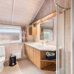 Bathroom with shower, sink, and toilet. White tiles and wooden ceiling.