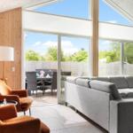 Wohnbereich mit grauem Sofa, orangefarbenen Sesseln und Blick auf den Garten.