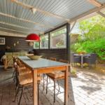 Terrasse mit Tisch, Stühlen und Blick auf grünen Garten. Decke mit Holzbalken und roter Lampe.
