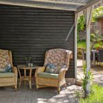 Zwei Stühle mit floralen Bezügen und ein kleiner Tisch stehen unter einer Veranda.