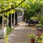 Hinterhof mit Terrasse, Gartenmöbeln und Pflanzen. Schwarzes Holzhaus mit Veranda.