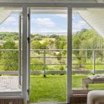 Durch große Fenster blickt man auf einen grünen Garten und Wald.