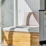 Sitzbank mit Kissen und Buch vor großem Fenster.
