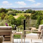 Balcony with two chairs and table, overlooking greenery and water.
