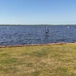 Windsurfer auf dem Wasser mit rotem Segel und weiterer Person im Hintergrund.