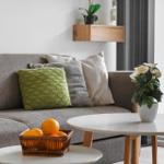 Grauer Sofa mit Kissen, runder Tisch, Obstkorb und Pflanzen.