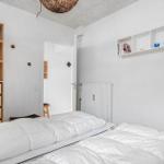 Schlafzimmer mit weißem Bett, Holzregal und Wandregal mit Büchern und Tassen.
