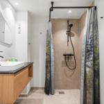 Badezimmer mit Dusche und Waschtisch. Duschvorhang zeigt Waldmotiv.