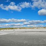 Strand mit Sanddünen und blauem Himmel mit weißen Wolken.