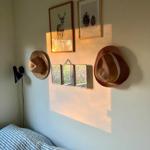 Wand mit zwei Bildern, zwei Hüten und drei Spiegeln über einem Bett mit gestreifter Bettwäsche.