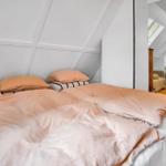 Bedroom with double bed, light walls, and sloped ceiling. Passage to another room.