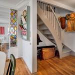 House with wooden floor, staircase, and colorful glass window. Jacket and hats hang on the wall.