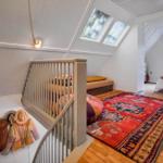 Bedroom with sloped ceiling, windows, and hardwood floor. Staircase with railing and rug.