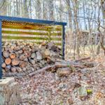 Stack of firewood under a wooden shelter in the woods.
